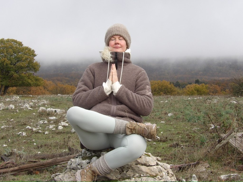 Anja sidder i meditation i et åbent naturlandskab
